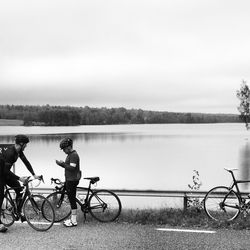 People on bicycles by lake against sky