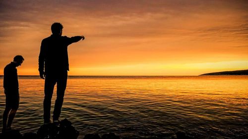 Silhouette man standing by sea against sky during sunset