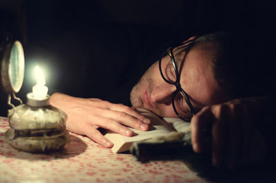Man sleeping on book by illuminated oil lamp on table