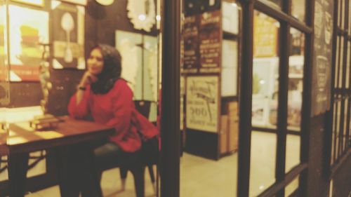 Woman looking through window while sitting on table