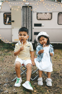 Asian multiracial kids girl and boy eat meat on a barbecue on a picnic in woods in summer on a trip