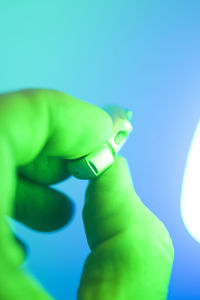 Close-up of hand holding leaf against blue background