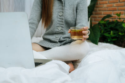 Midsection of woman holding drink on bed at home