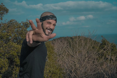 Side view portrait of smiling mid adult man gesturing in forest against sky