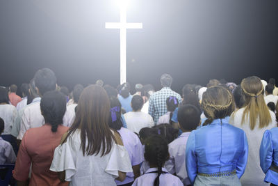 Crowd standing in front of illuminated cross at night