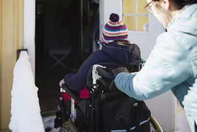 Woman pushing disabled person on wheelchair through entrance door