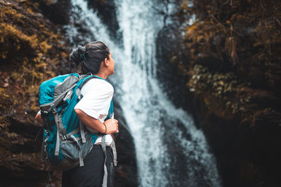 Rear view of man looking at waterfall in forest