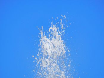 Low angle view of splashing water against clear blue sky