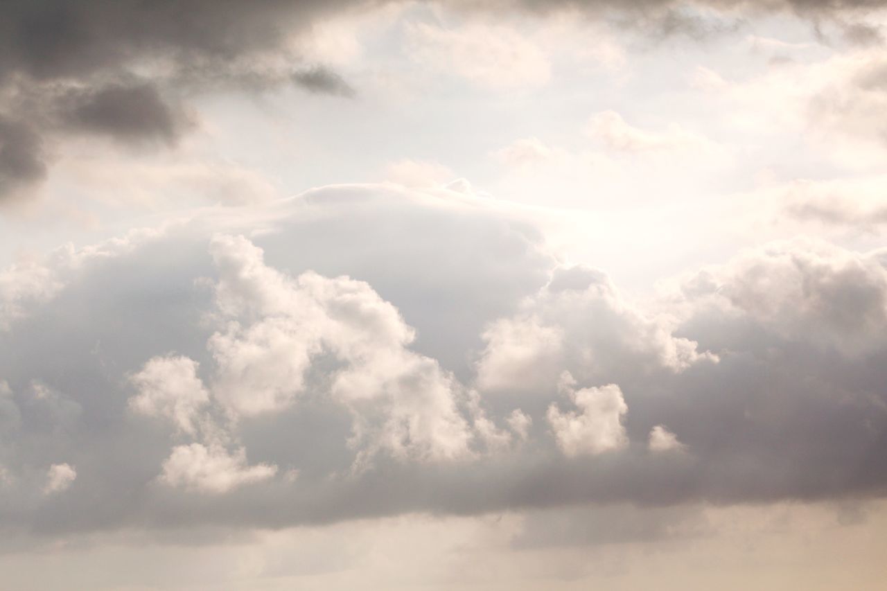 LOW ANGLE VIEW OF SUN STREAMING THROUGH CLOUDS IN SKY