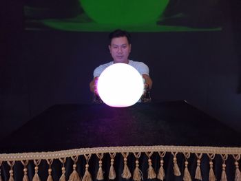 Full length of a young man holding ball while standing against illuminated wall