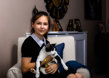 Portrait of smiling teenage girl with cat sitting at home