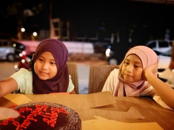 Sisters sitting with cake at table during night