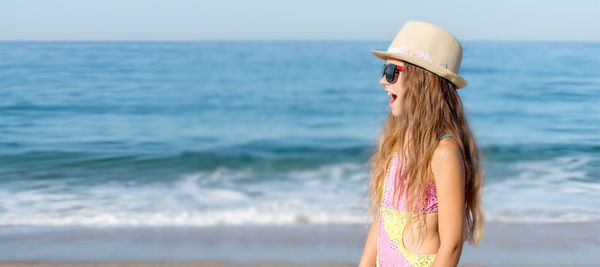 Side view of a girl with an open mouth against the background of the sea and sand.