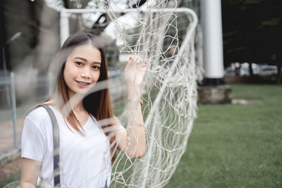 Portrait of young woman standing behind goal post on soccer field