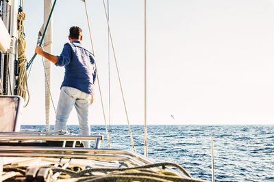 Rear view of man standing on boat in sea against clear sky