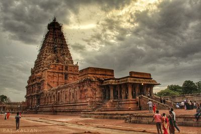 People at historical building against cloudy sky