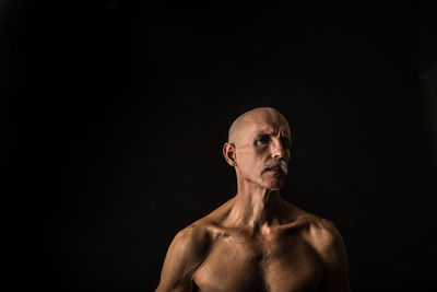 Portrait of shirtless mature man against black background