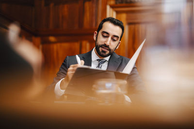 Confident bearded businessman with contract file sitting in board room during meeting