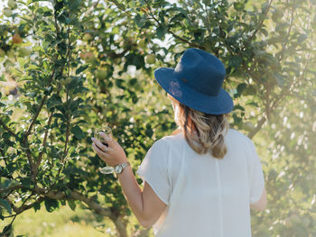 Young millennial woman outdoors in apple orchard having a glass of red wine with fedora hat on