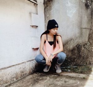 Full length of young woman sitting against wall