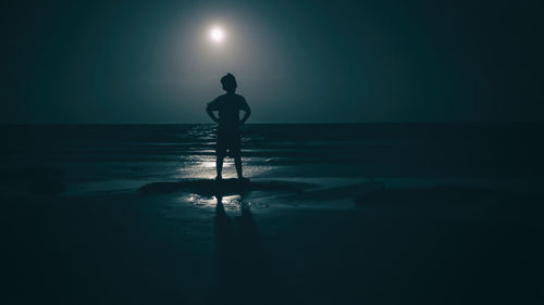 Silhouette boy standing at beach against sky during night