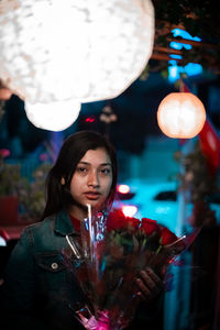 Portrait of young woman holding flowers at night