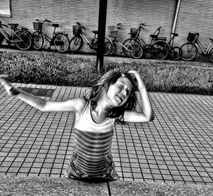 Sunlight falling on girl standing on footpath against bicycles parked by wall