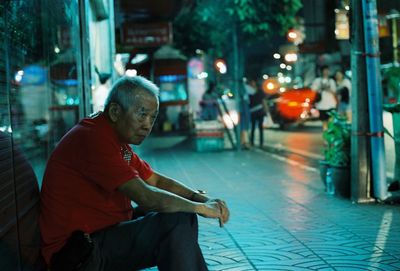 Man sitting on sidewalk in city at night