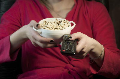 Midsection of woman having popcorn while changing tv channel