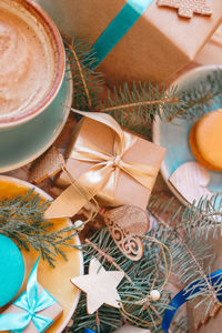Top view on gifts with christmas decorations on a table with blue cup with cappuccino and macarons.