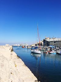 Sailboats moored on harbor against clear blue sky