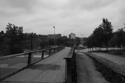 Footpath by trees on city against sky