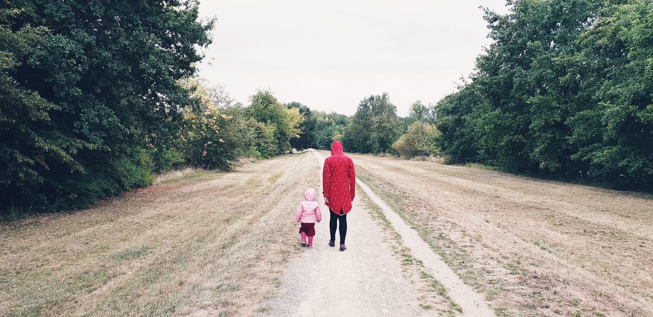 REAR VIEW OF WOMAN WALKING ON ROAD ALONG TREES