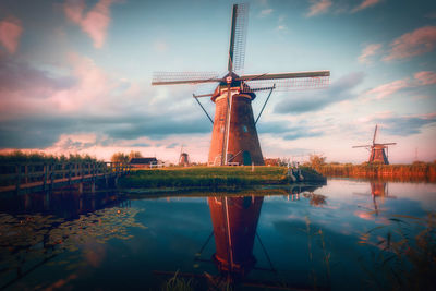 Traditional windmill by lake against sky