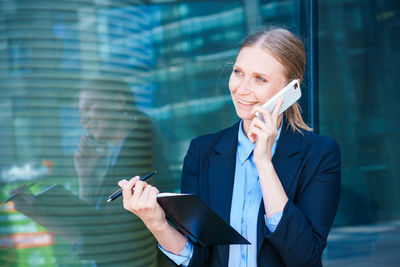 Woman in business suit carries folder with documents and smiles while talking