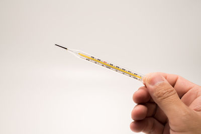 Close-up of hand holding thermometer against white background