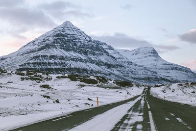 Snow covered road by mountain against sky