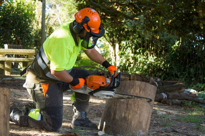 Forest worker cutting logs with chainsaw