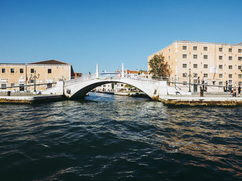 Bridge over river in city against clear blue sky