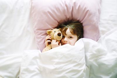 Directly above portrait of cute boy with teddy bear lying on bed at home