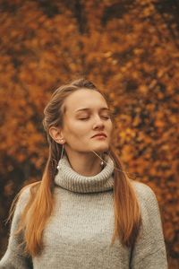 Portrait of beautiful woman standing against orange autumn leaves