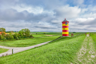 Lighthouse on field by building against sky