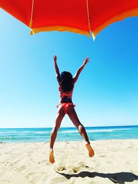 Rear view of woman jumping at beach against clear sky