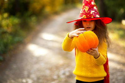 Cute girl wearing hat holding pumpkin outdoors