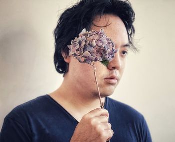 Portrait of young asian man holding stalk of purple hydrangea flowers on white background.