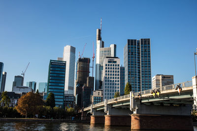 Bridge over river by buildings against clear sky