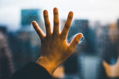 Close-up of hand touching wet glass window