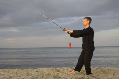 Man practicing tai chi at beach against cloudy sky