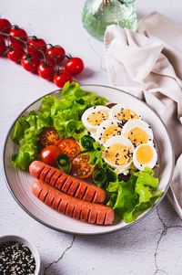 Plate with sausages, egg sandwich, tomatoes and lettuce leaves on the table vertical view