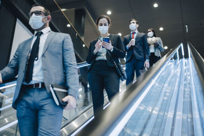 Male and female entrepreneurs moving downwards on illuminated escalator during pandemic